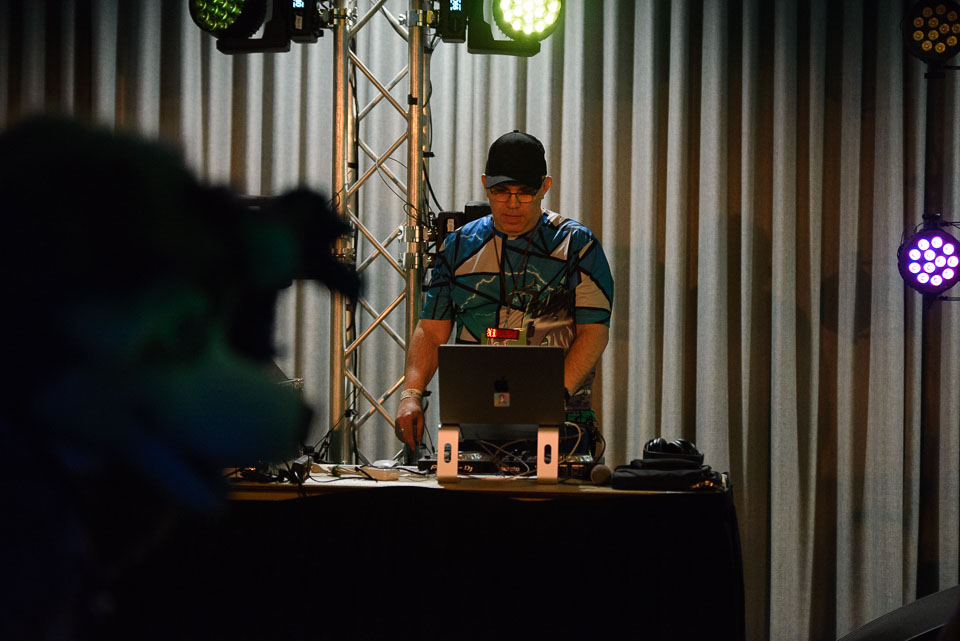 DJ standing at DJ table with fursuiter in foreground.